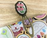 Oval bookmark with floral embroidery sits on a wooden table and a colorful book page.
