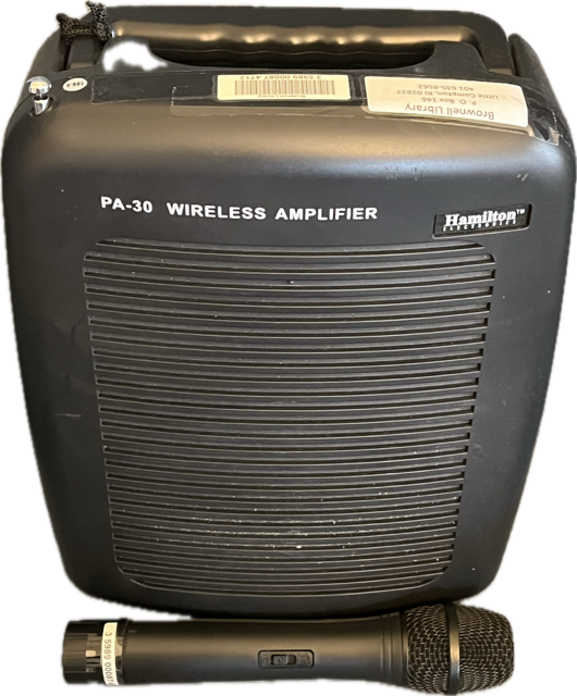 Black wireless amplifier with a microphone placed in front of it on a white background.
